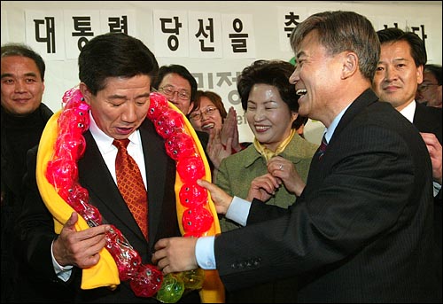 2002년 12월 20일 김원웅 개혁당 의원이 노무현 대통령 당선자에게 돼지저금통으로 만들어준 화환을 걸어주며 축하하고 있다. 